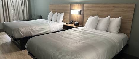 A hotel room with two beds, a cityscape painting, a nightstand with a lamp, and a view of the city through the window.