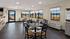 Un comedor amplio con varias mesas y sillas, ventanas grandes que ofrecen vistas al exterior y un equipo de aire acondicionado instalado.