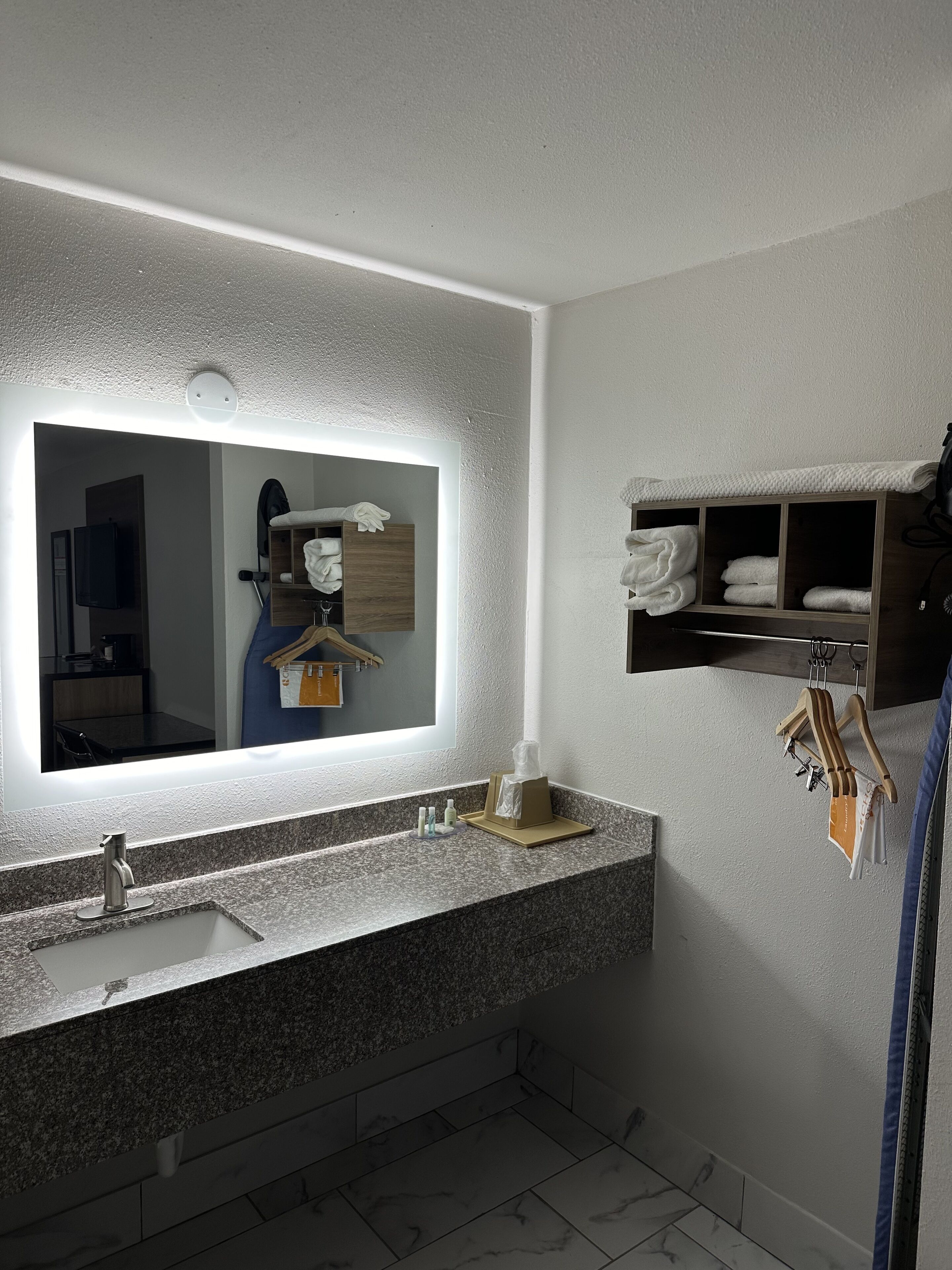 A modern bathroom with a large mirror, granite countertop, and a towel rack with folded towels.