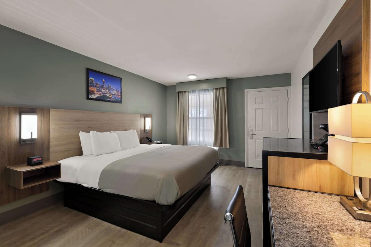 A hotel room with a large bed, a desk with a lamp, a TV, and a painting on the wall.
