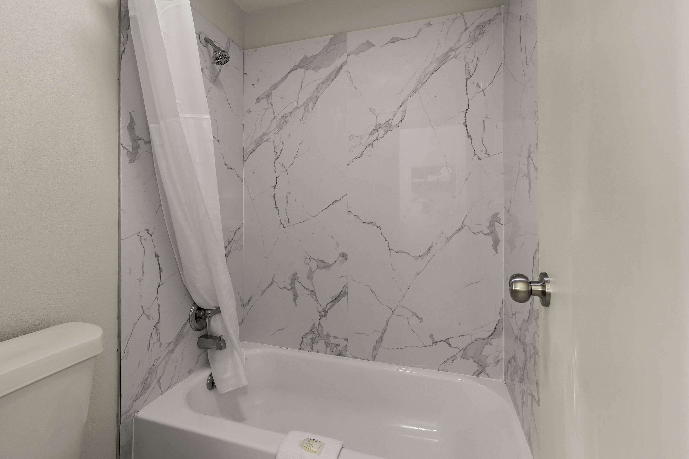Un baño con pared de mármol, bañera y cortina de ducha.