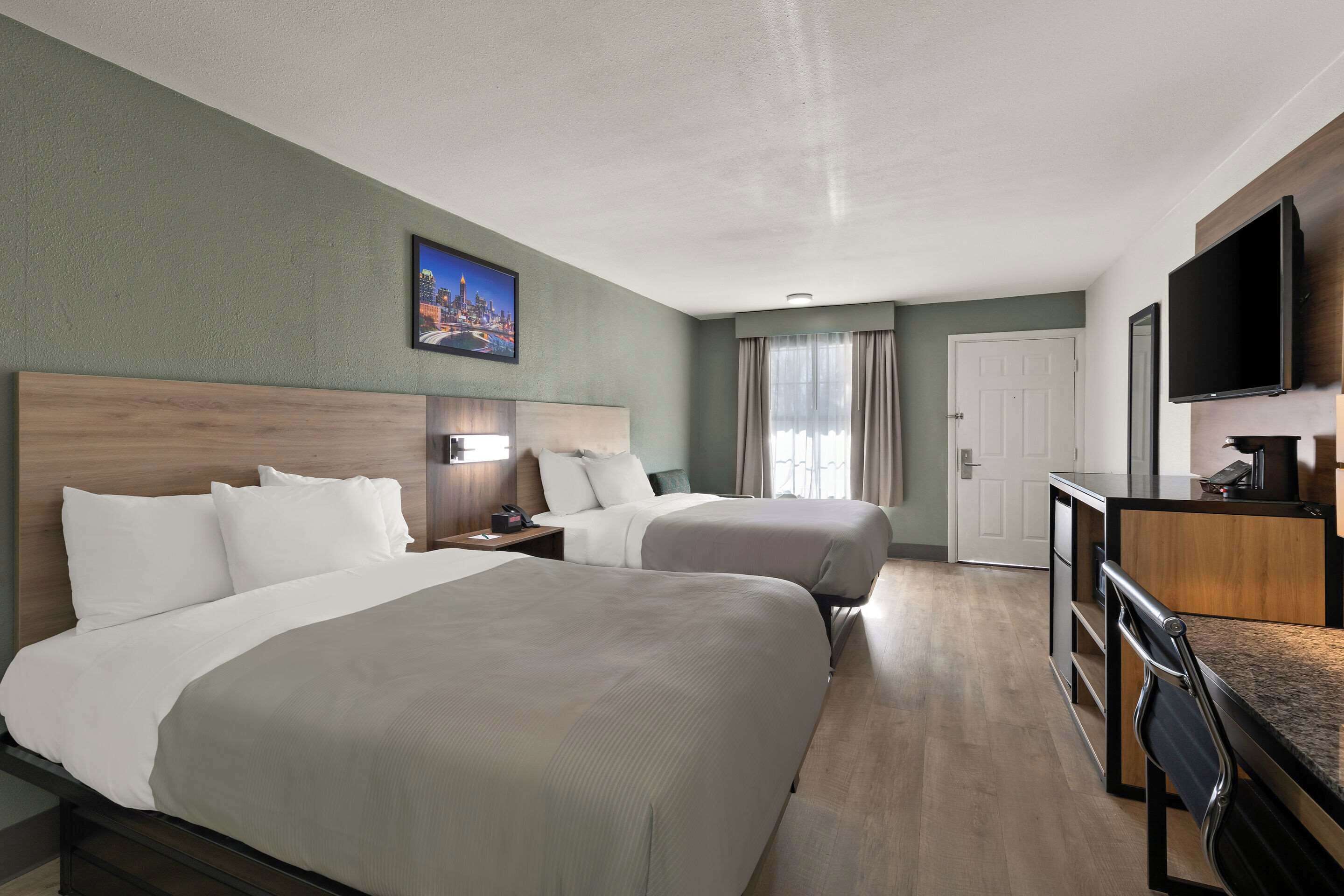 Una habitación de hotel con dos camas, un escritorio, un televisor y un cuadro en la pared.