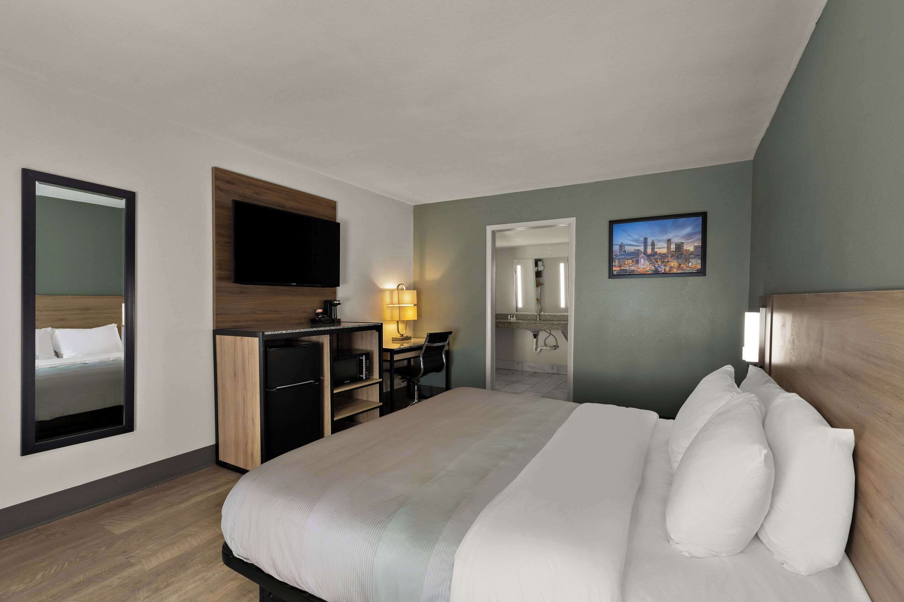 Habitación de hotel con cama, escritorio, televisor y baño visible a través de una puerta abierta.