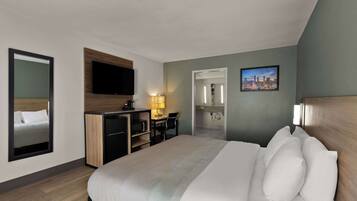 Habitación de hotel con cama, escritorio, televisor y baño visible a través de una puerta abierta.