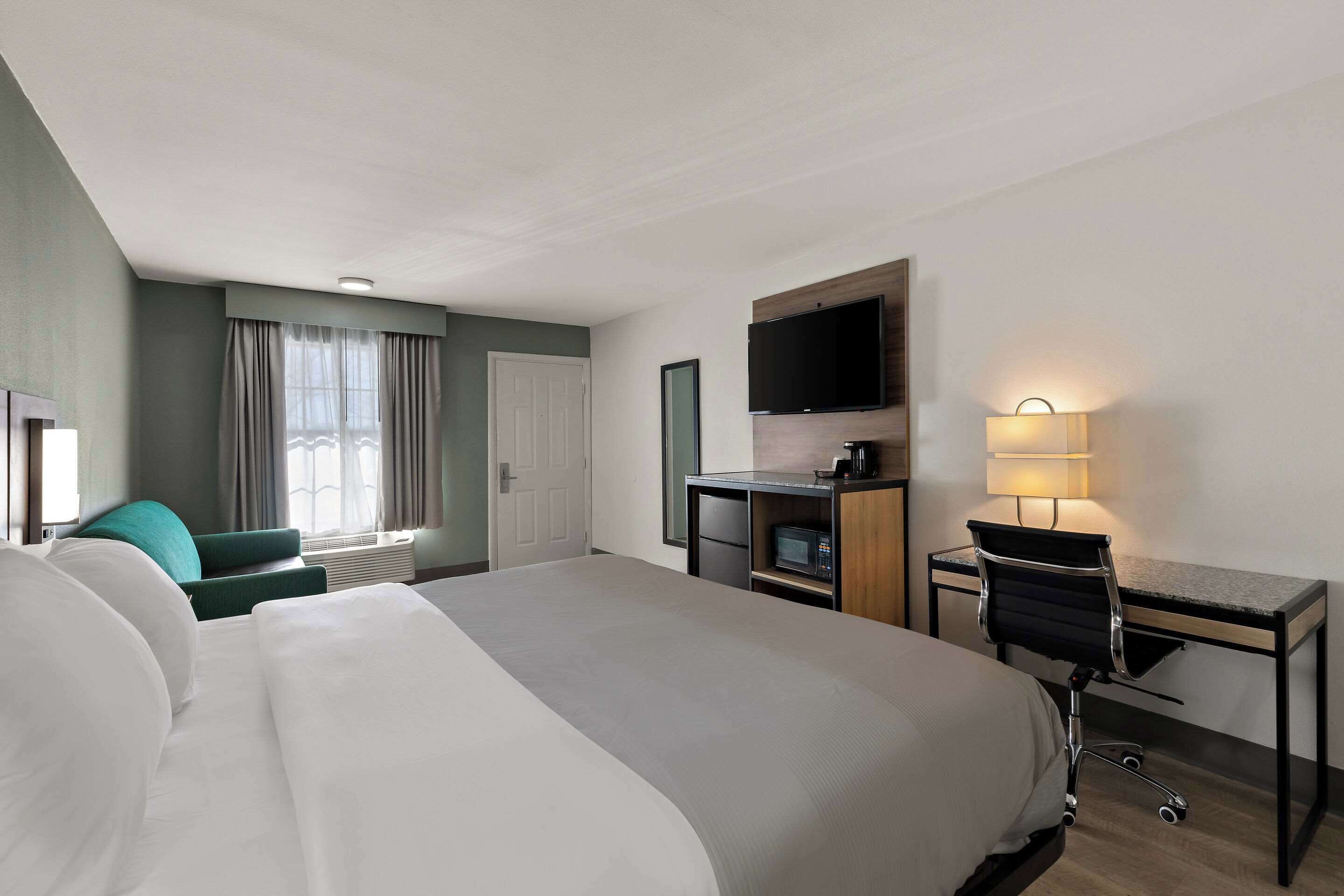 A hotel room with a large bed, a desk with a chair, a television, and a lamp.