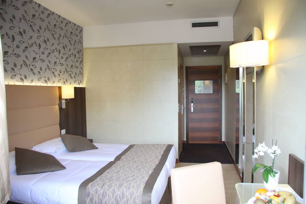 A hotel room with a bed, a chair, a table with flowers, and a door leading to another room.