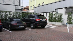 A parking area with two cars, a building with a yellow facade, and a brick pathway. - LH Hotel Sirio Venice (Mestre)