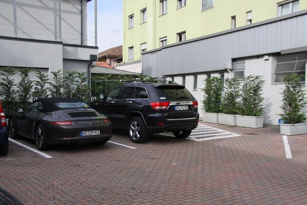 A parking area with two cars, a building with a yellow facade, and a brick pathway. - LH Hotel Sirio Venice (Mestre)