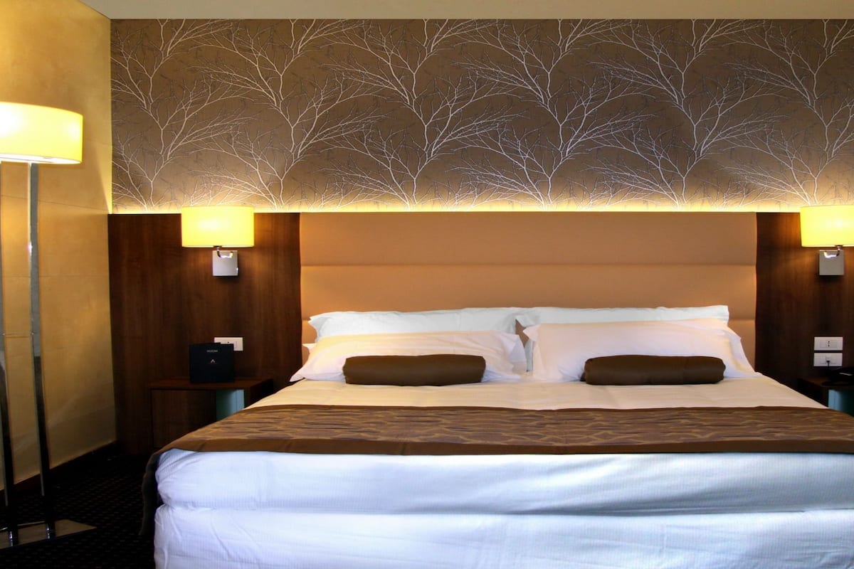A hotel room with a large bed, two bedside tables, a wall-mounted lamp, and a decorative tree pattern on the ceiling.