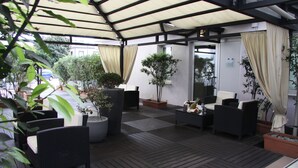 An outdoor patio area with wicker furniture, potted plants, and a covered seating area. - LH Hotel Sirio Venice (Mestre)