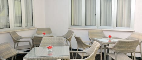 Un patio amueblado con mobiliario de mimbre y mesas de vidrio, con amplias ventanas con cortinas.