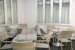 A patio area with wicker furniture and glass tables, featuring large windows with curtains. - LH Hotel Sirio Venice (Mestre)