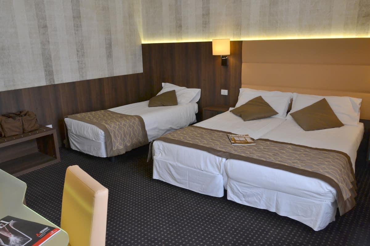 A hotel room with two single beds, a desk, and a chair.