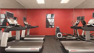 A gym with treadmills, stationary bikes, and a mirrored wall.