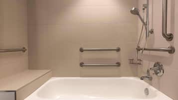 A bathroom with a white bathtub, grab bars, and a showerhead.