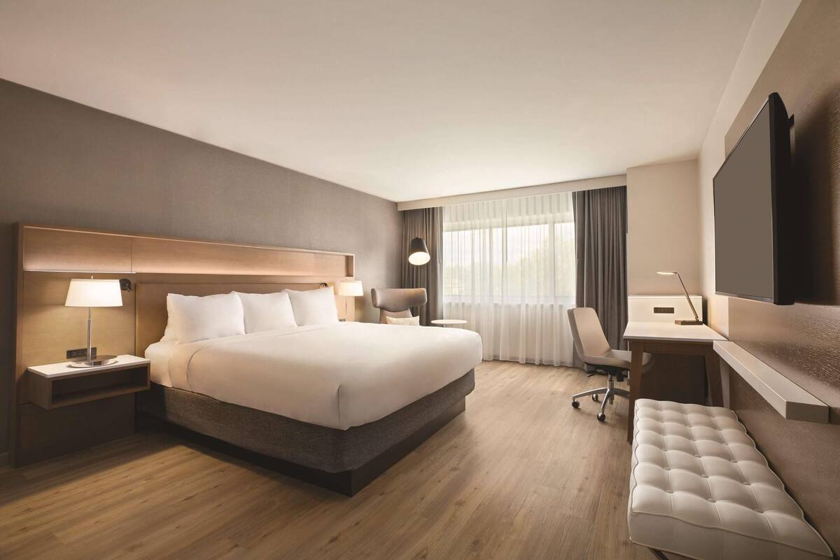 A hotel room with a large bed, bedside tables, a desk, a chair, and a TV.