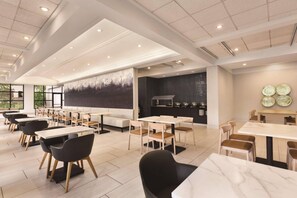 A spacious dining area with multiple tables and chairs, a large abstract painting on the wall, and a modern ceiling design. - Radisson Hotel Seattle Airport (SeaTac)
