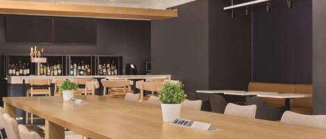 A modern conference room with a long table, chairs, a bar area with bottles, and a potted plant.