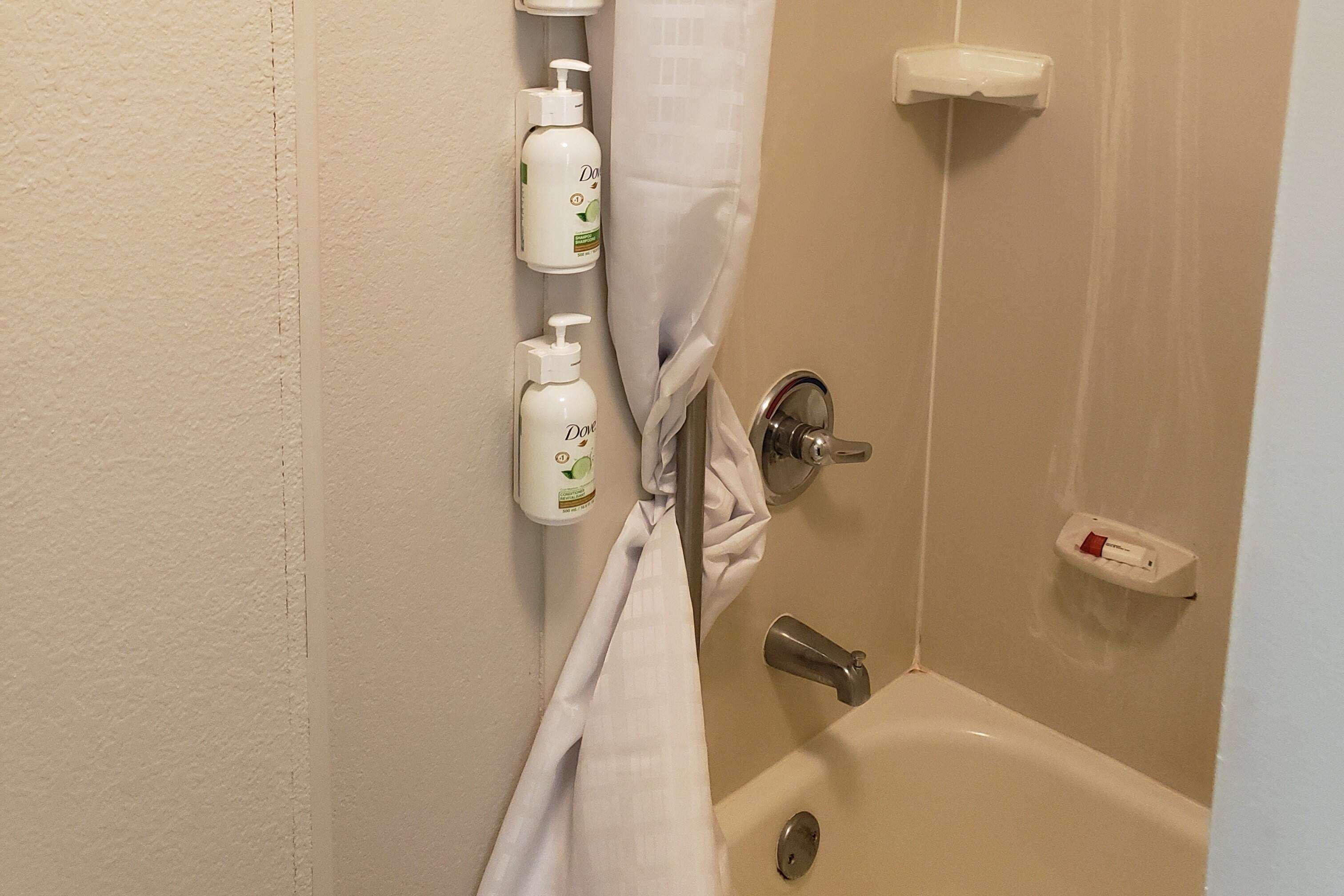 A bathroom with a bathtub, a towel rack with bottles, and a shower curtain.