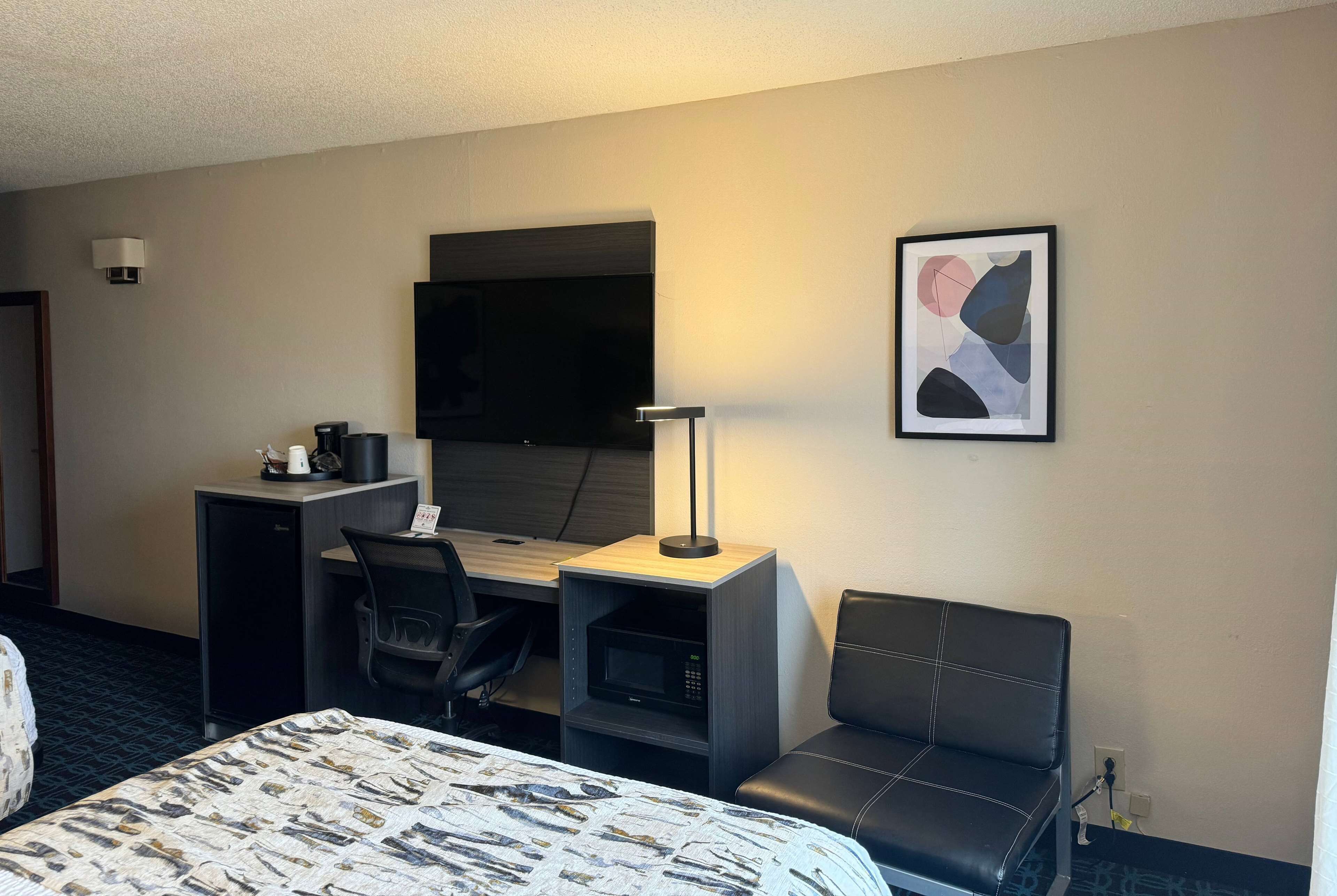 A hotel room with a bed, a desk with a computer, a chair, a television, and a framed picture on the wall.