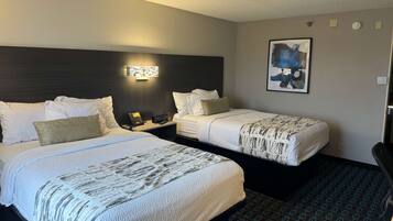 A hotel room with two beds, a nightstand with a phone, a wall-mounted light, and a framed abstract painting.