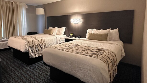 A hotel room with two beds, a bedside table with a lamp, a telephone, and a wall-mounted light fixture. - Wingate by Wyndham Dayton North (Dayton)