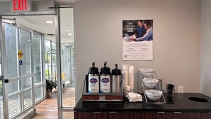A coffee station with dispensers, a sign for automatic caution doors, and a poster on the wall. - Wingate by Wyndham Dayton North (Dayton)