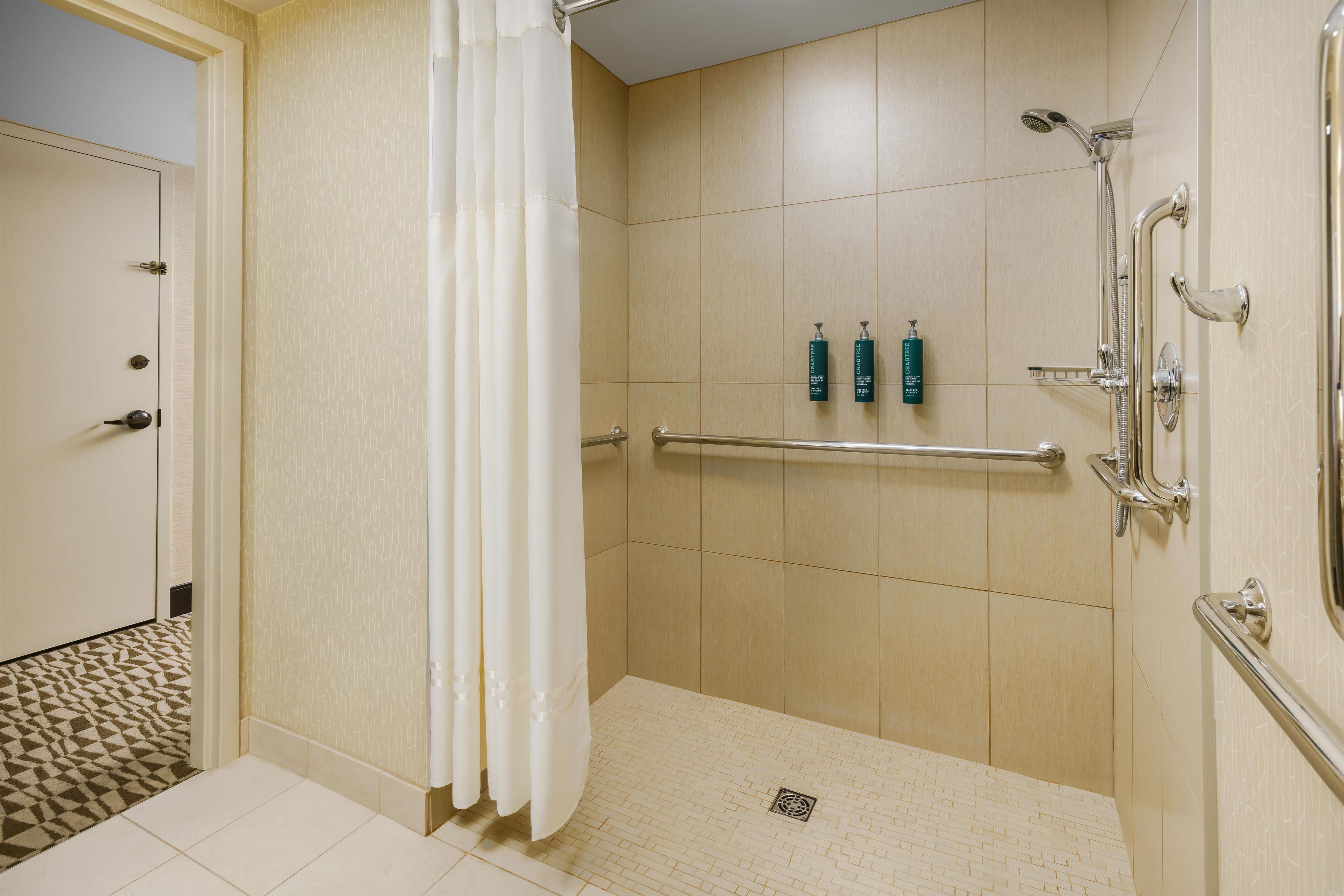 A shower area with a grab bar, a towel rack, and two bottles of GrabTree shampoo.