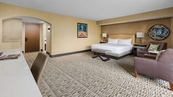 Una habitación de hotel con una cama, un escritorio, una silla, un sofá, una lámpara y un cuadro en la pared.