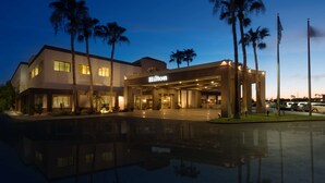 A modern hotel with a well-lit entrance, palm trees, and a reflection pool. - Hilton Phoenix Airport (Phoenix)