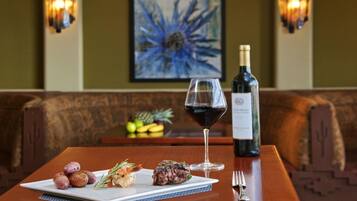 A dining table with a plate of food, a glass of red wine, and a bottle of wine.