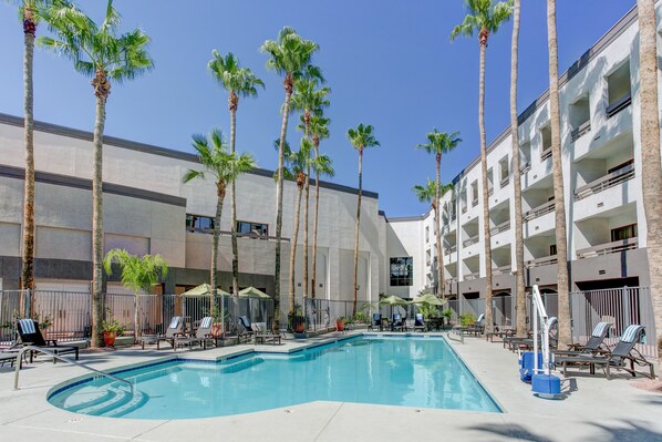 A pool area with lounge chairs, palm trees, and a building with balconies. - Hilton Phoenix Airport (Phoenix)