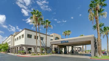 A modern hotel with a covered entrance, palm trees, and a clear blue sky.