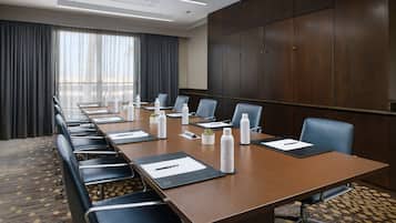 A conference room with a long table, multiple chairs, water bottles, and a large window with curtains.