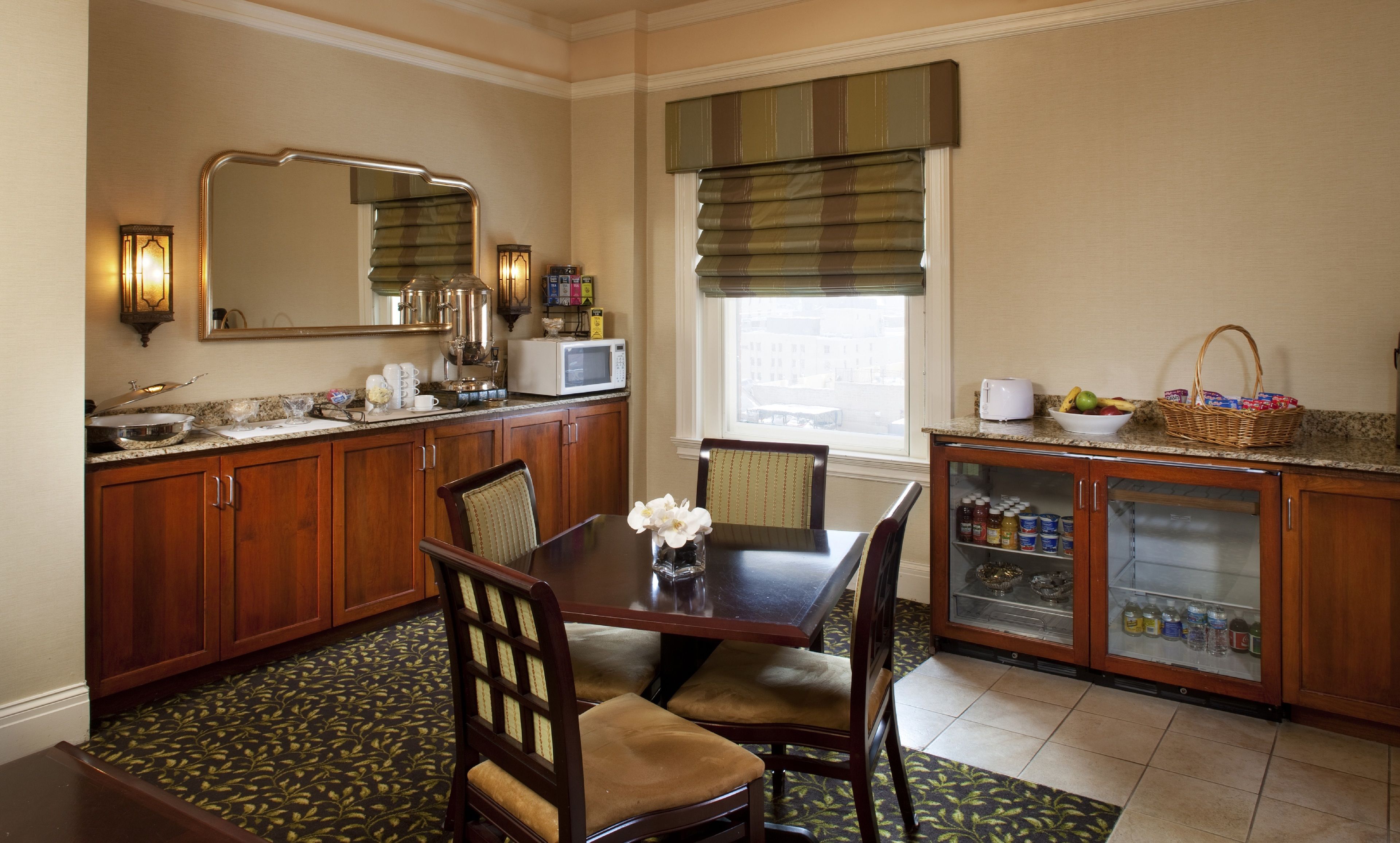 A dining area with a wooden table, chairs, a vase with flowers, and a buffet cabinet with food items.