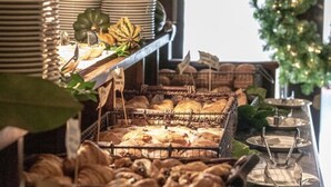 Une vitrine de boulangerie présentant des pâtisseries et du pain, un coin café et, au fond, un sapin de Noël.