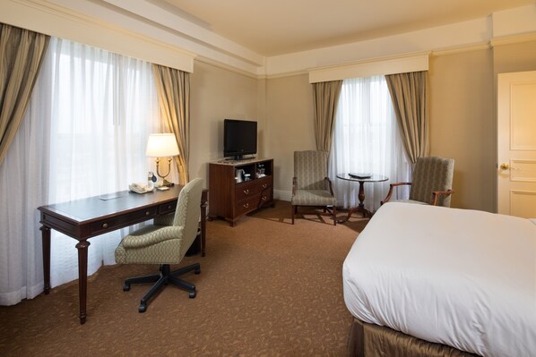 Habitación de hotel con una cama grande, un escritorio con silla, un televisor, una mesita y dos sillas.