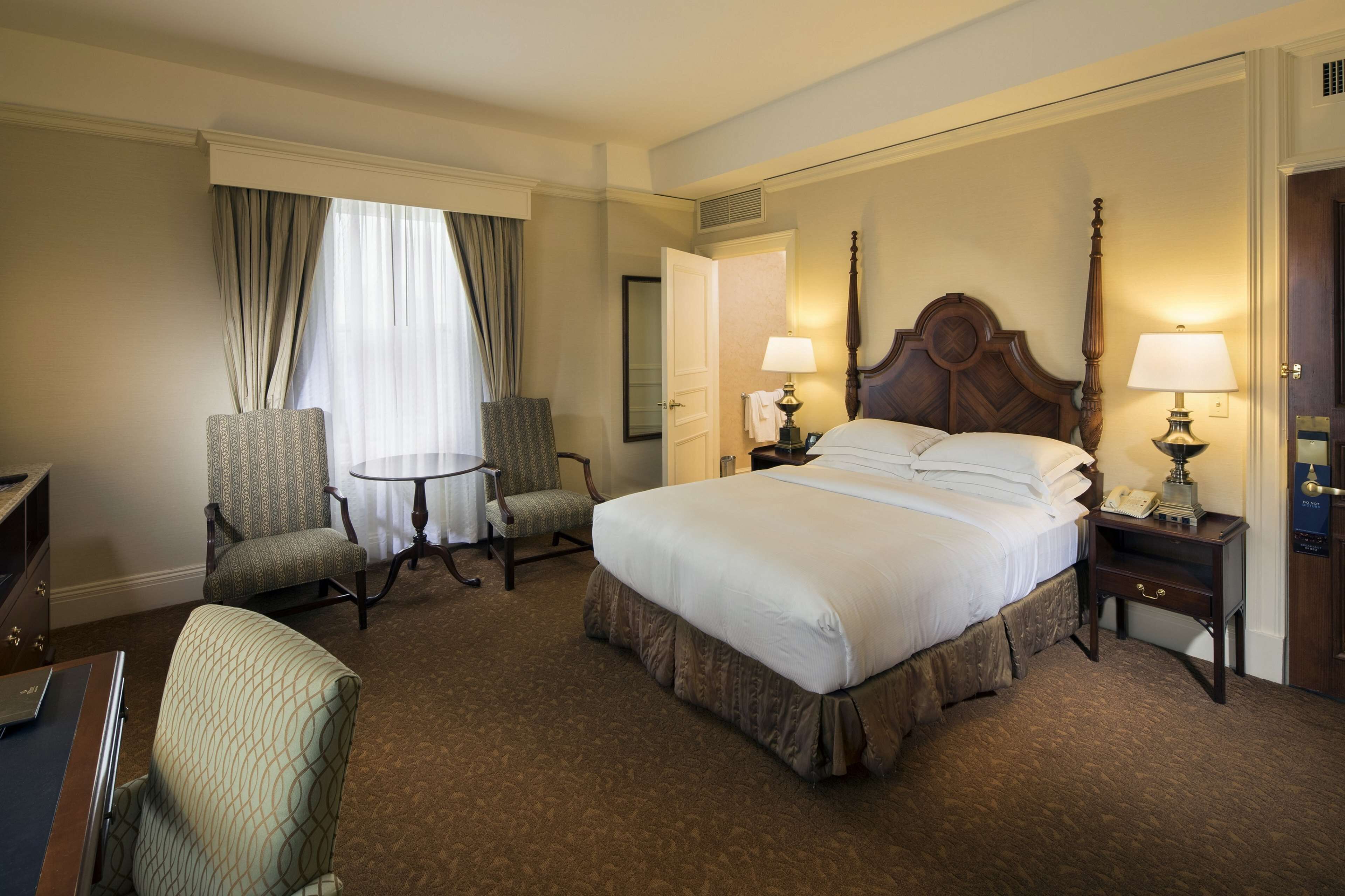 Una habitación de hotel con una cama grande, dos sillones, un escritorio y una mesita.