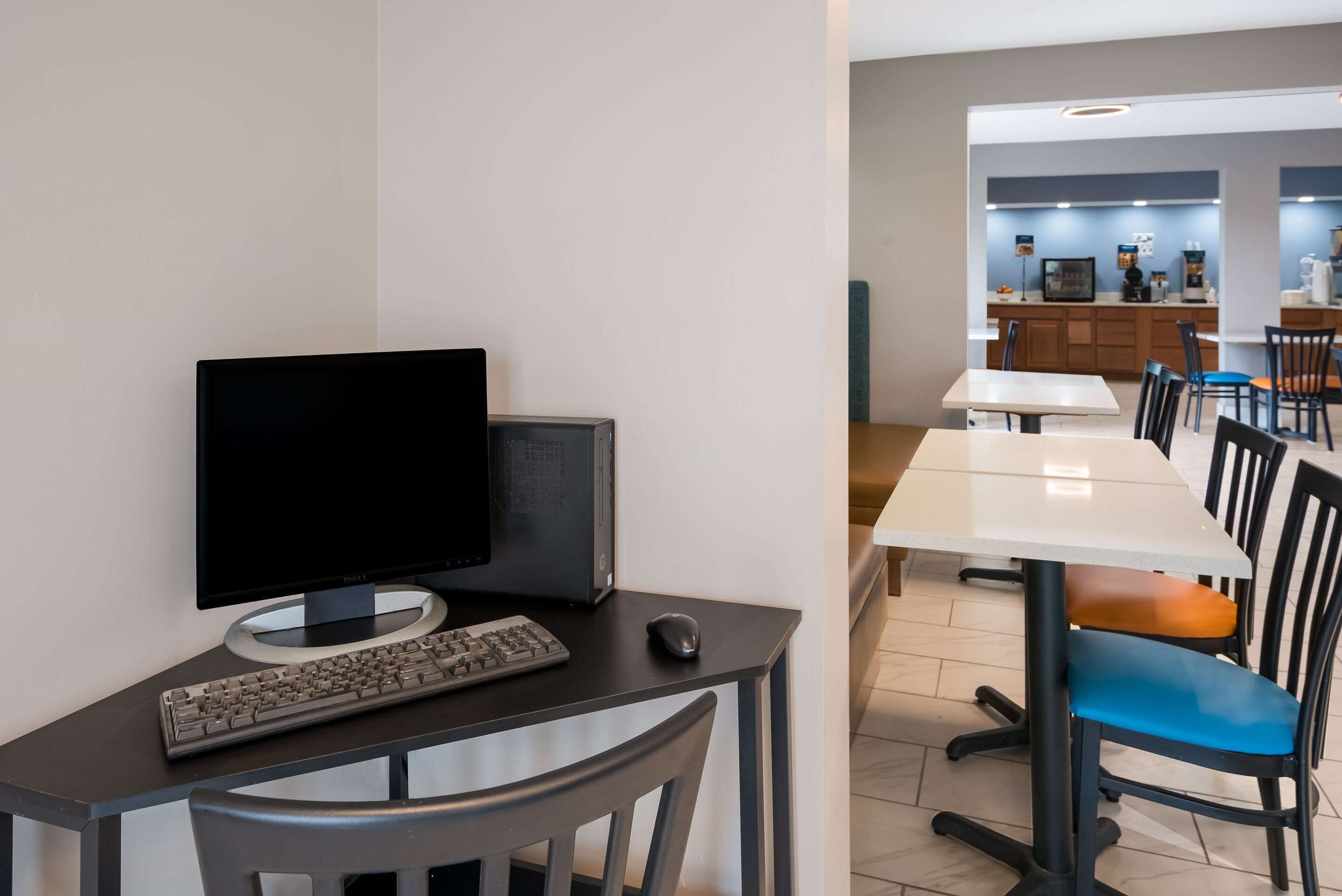 A modern dining area with a computer setup, a white table, and chairs with blue and orange cushions.