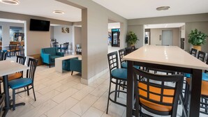 A modern dining area with a long table and chairs, a sofa, and a television on the wall. - Clarion Pointe Indianapolis Northeast (Indianapolis)
