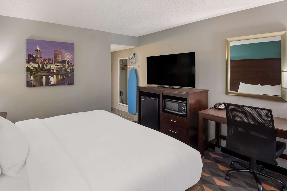 A hotel room with a bed, a desk with a computer, a television, and a cityscape painting on the wall.