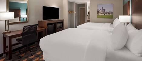 Habitación de hotel con dos camas, un escritorio con computadora, televisión y un cuadro con vista a la ciudad.