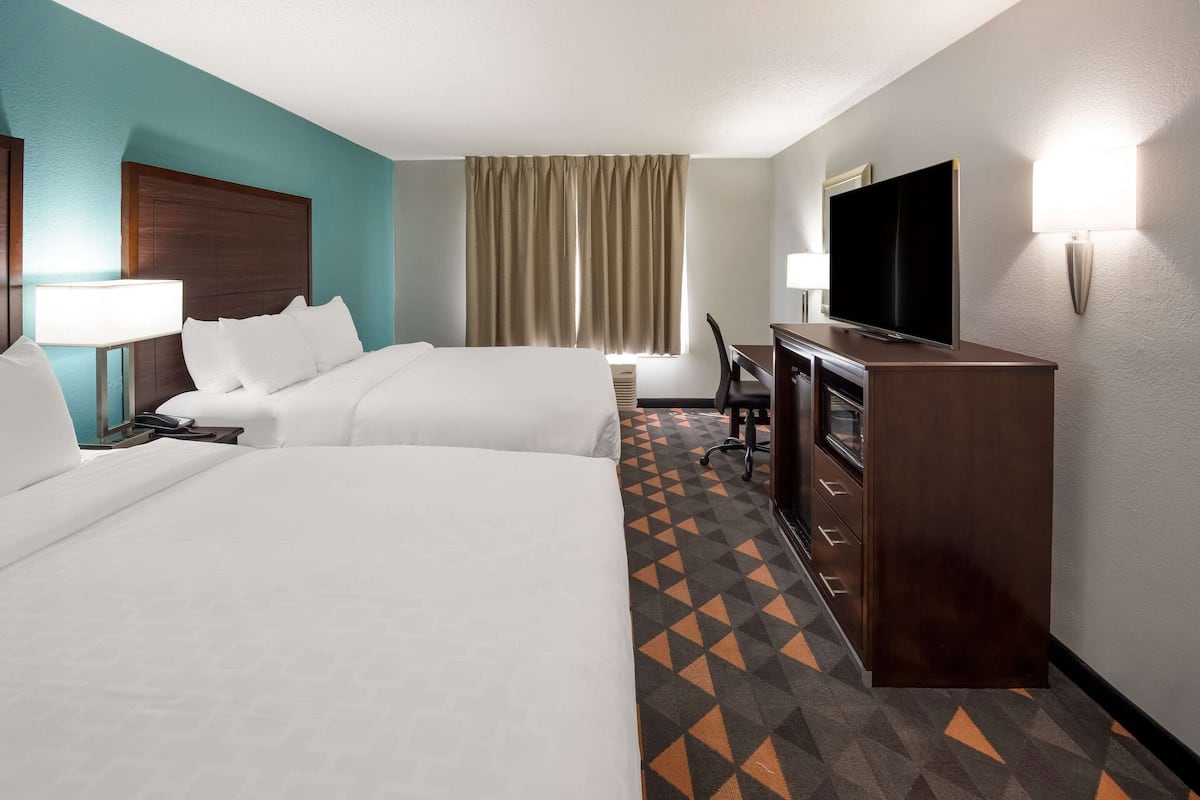 A hotel room with two beds, a desk with a TV, a lamp, and a window with curtains.
