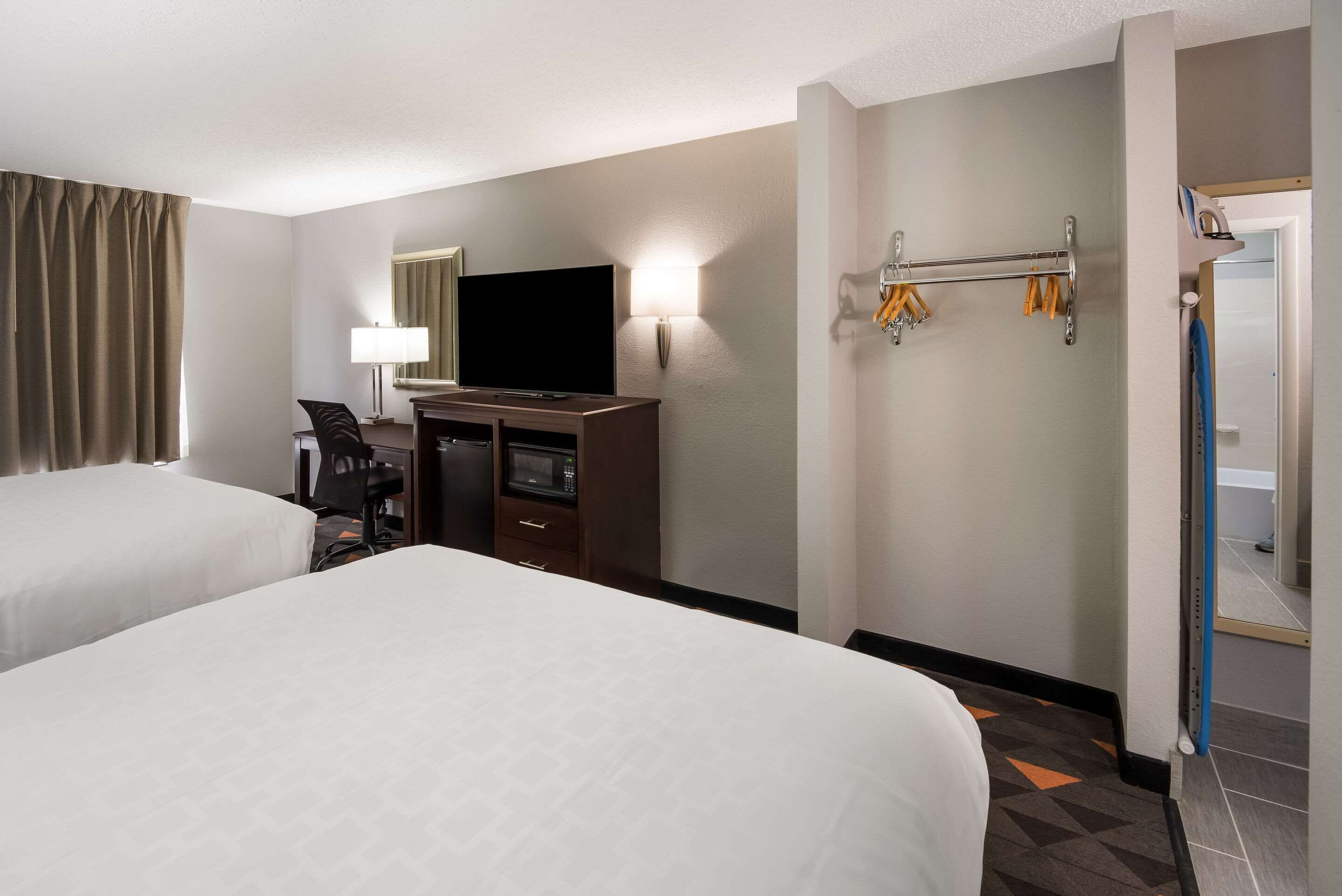 A hotel room with two beds, a desk with a computer, a TV, a lamp, and a coat rack.