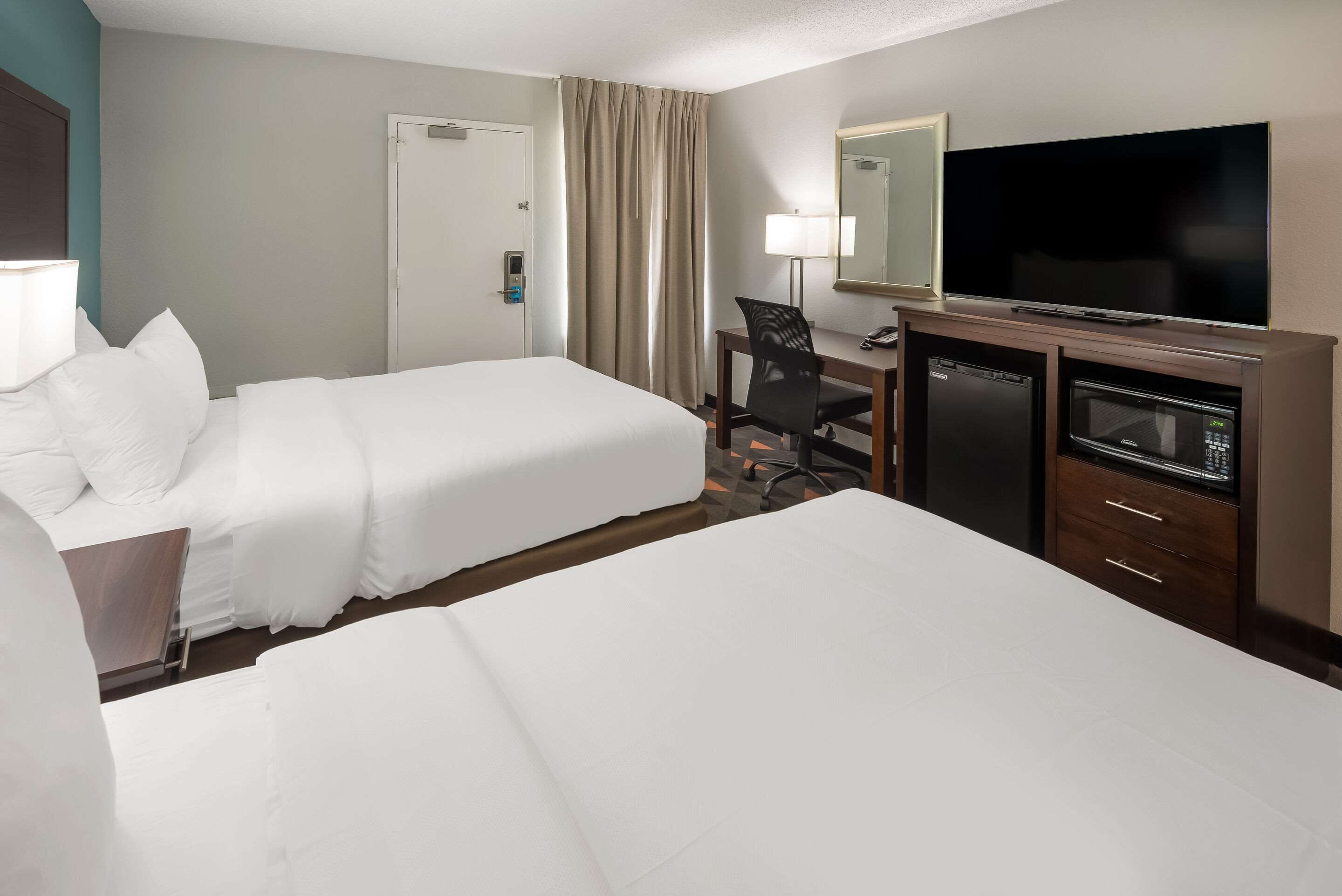 A hotel room with two beds, a desk with a computer, a TV, and a minibar.