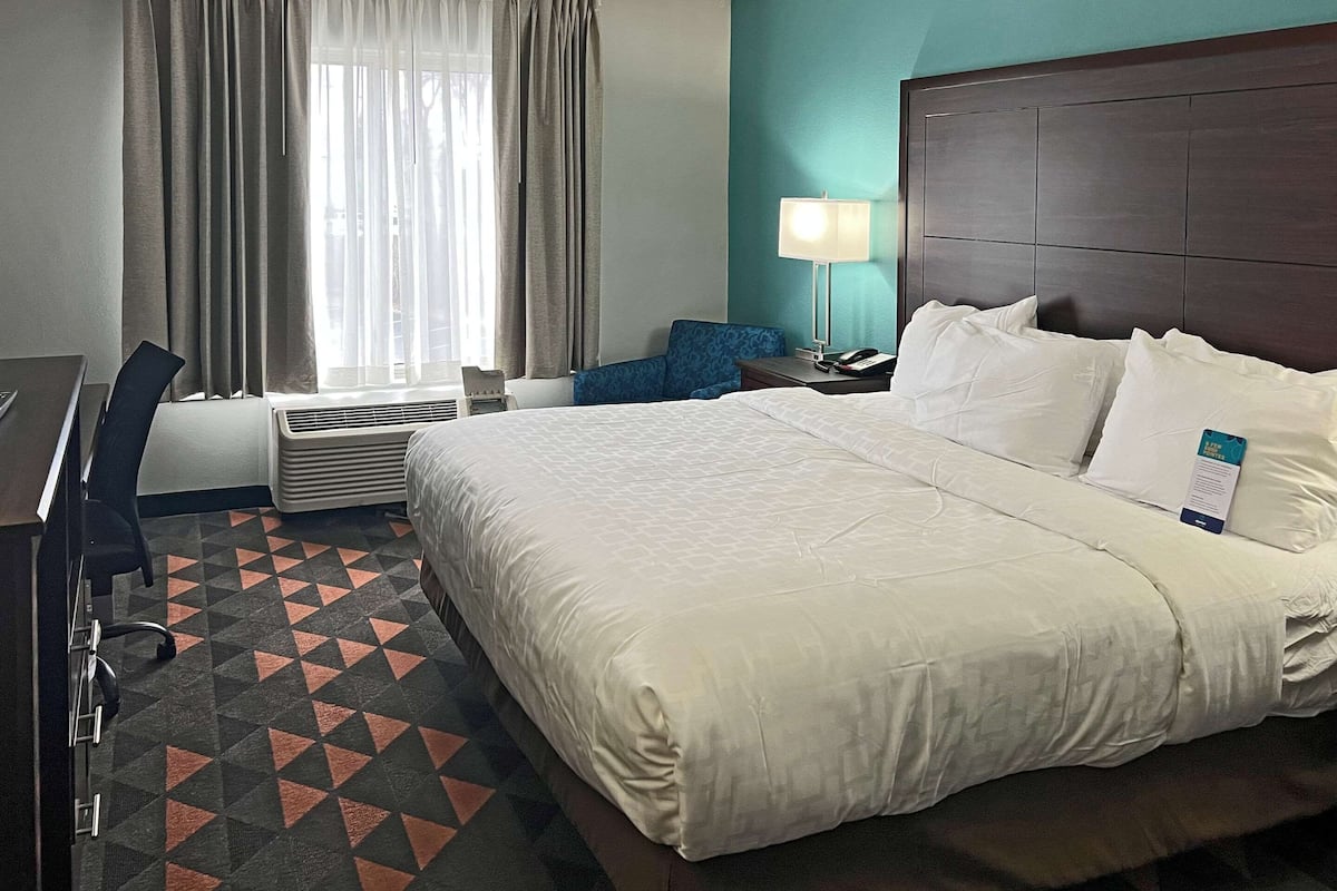 A hotel room with a large bed, a desk, a chair, a lamp, and a window with curtains.