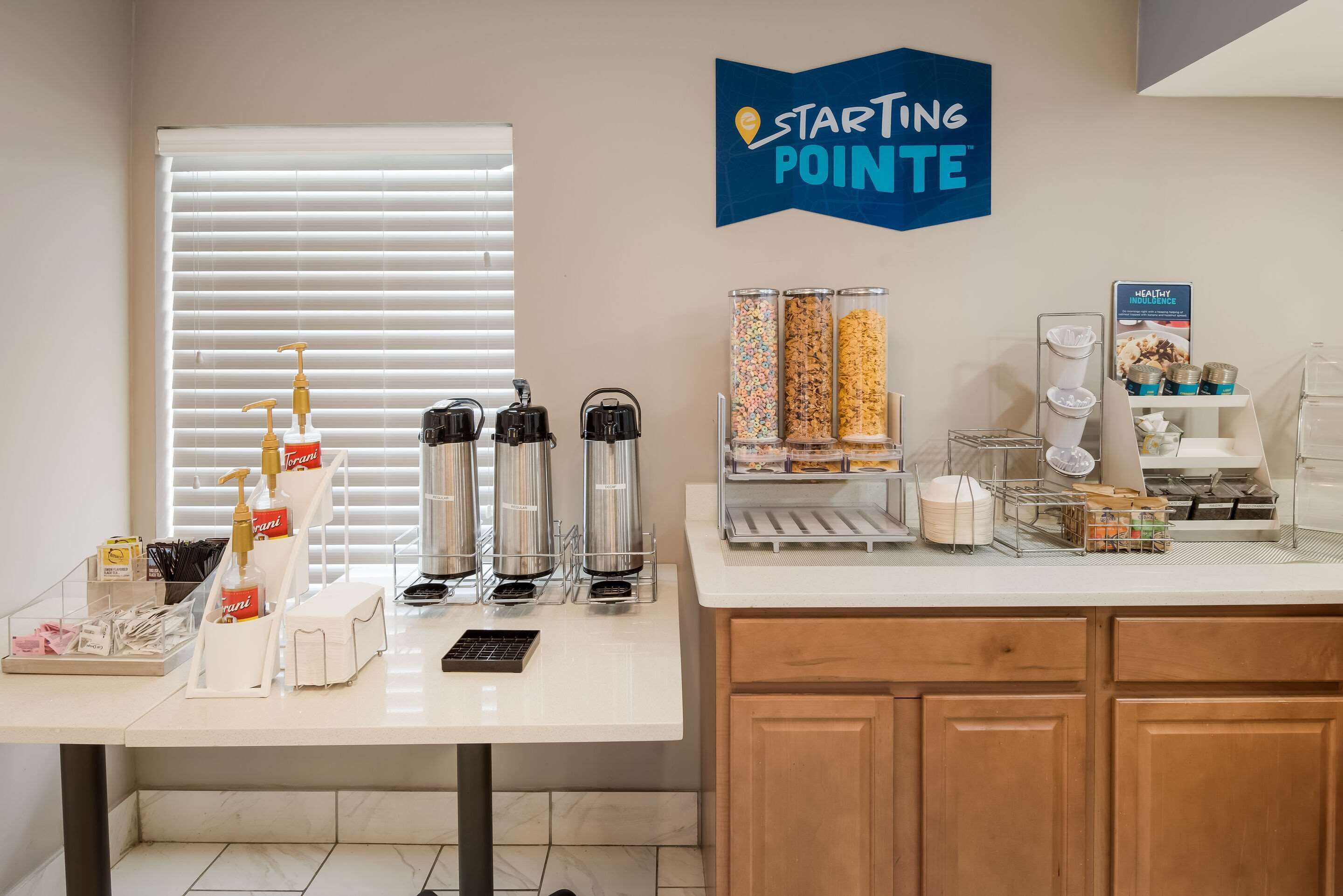 A clean, well-organized breakfast bar with dispensers, a coffee machine, and a variety of food containers.