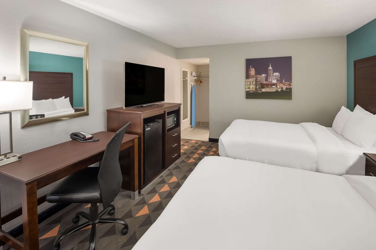 A hotel room with a bed, desk, chair, TV, and a cityscape painting.