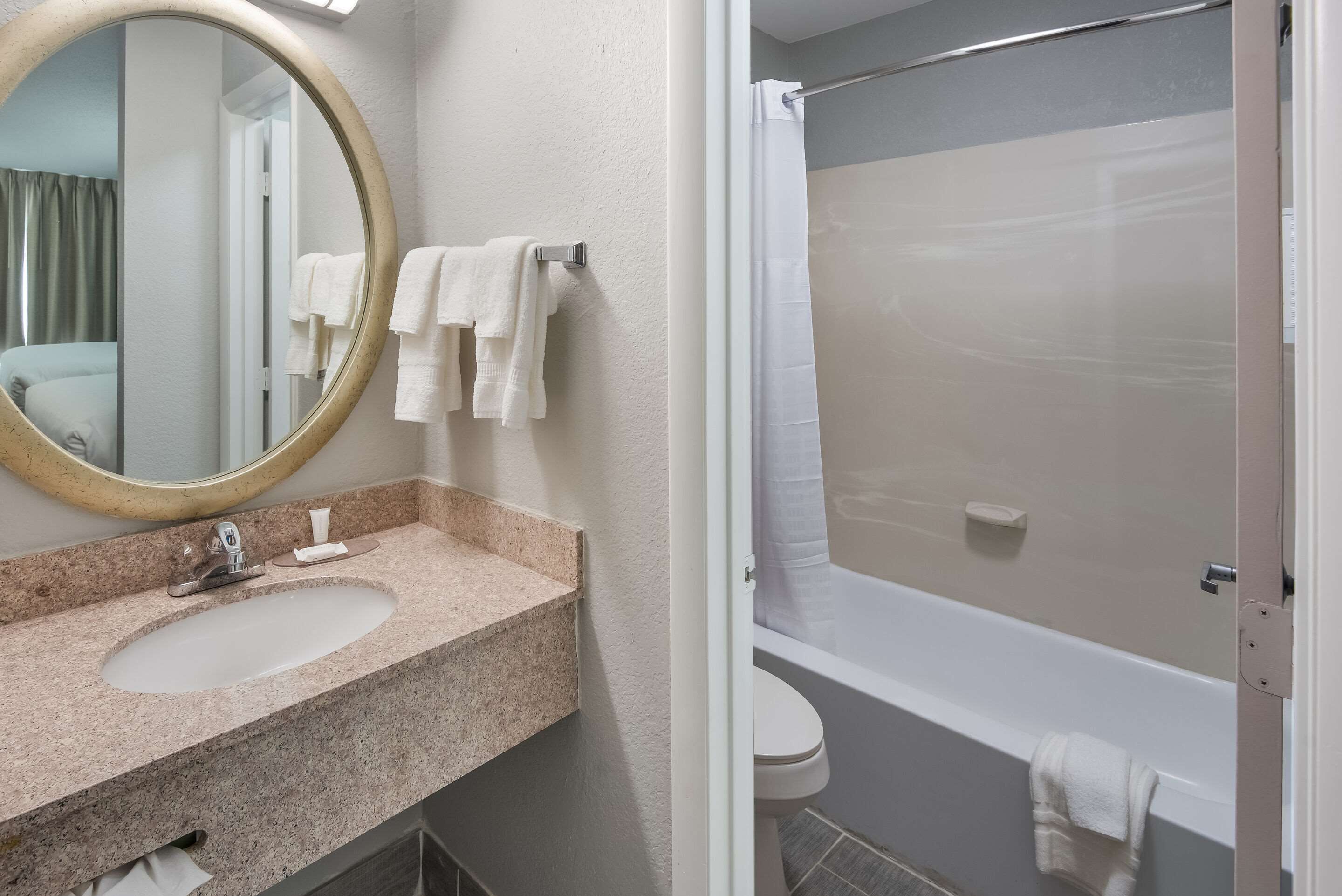 A bathroom with a granite countertop sink, a round mirror, and a shower with a glass door.