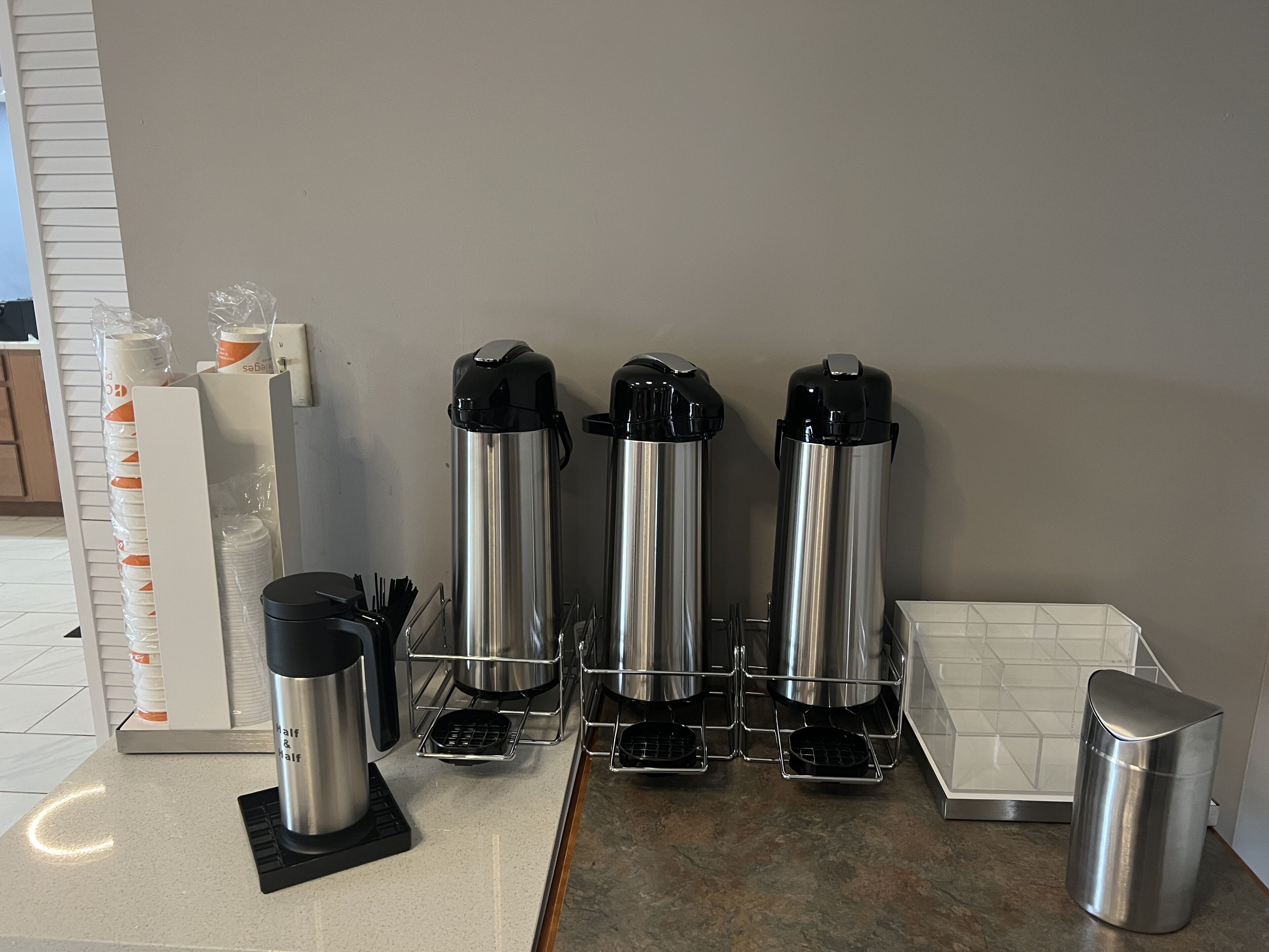 A kitchen counter with three stainless steel coffee makers and a smaller one, a coffee pot, and a metal container.